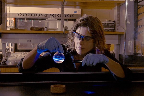 woman with gloves holding beaker with uv light